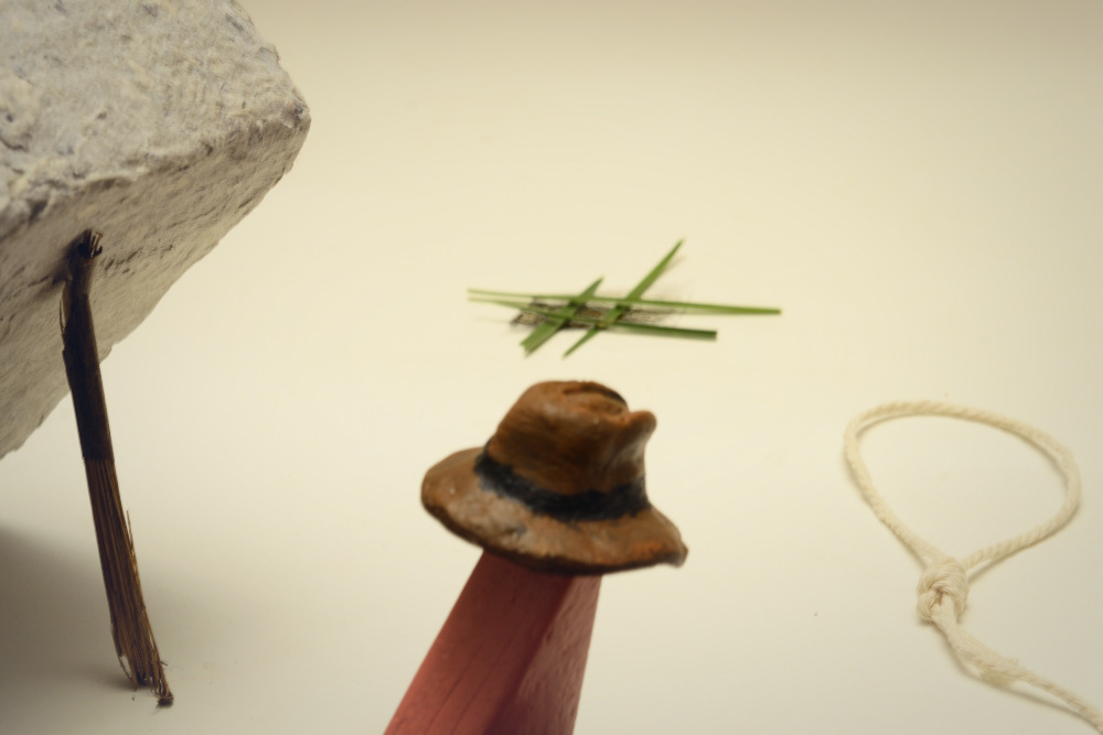 Block Woman is wearing a battered tan-colored wool hat. There are 3 traps nearby: a cement block; a lasso; a green jungle camouflage.