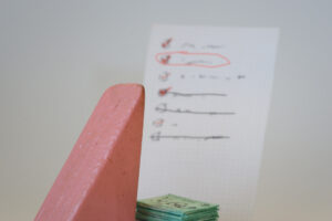 Block Woman reviews a hand-written list of potential charitable donations. There is a pile of cash underneath the list.
