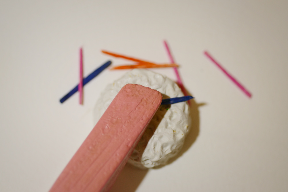 Block Women's head is lying on a round cake with white icing. Seven colorful birthday candles are strewn around.