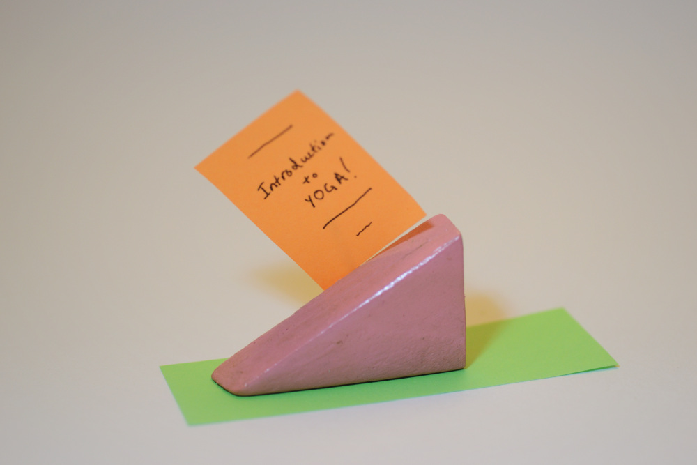 Block Woman is lying on a yoga mat which is shown as green strip of paper. There is an orange rectangle piece of paper that says Introduction to YOGA!