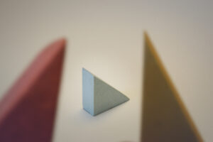 In the foreground, but blurred, are 2 partial Blocks, a pink one the left and a yellow one on the right. In the background but in focus is a small blue Block.