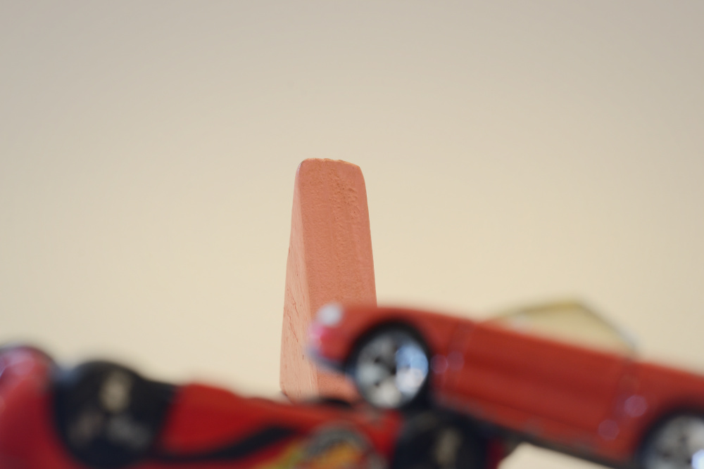 Block Woman stands in focus in the background with two blurry red cars in the foreground that have crashed into each other.