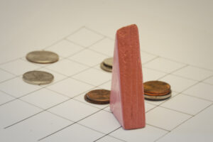 Block Woman surveys scattered piles of coins placed on a grid of squares