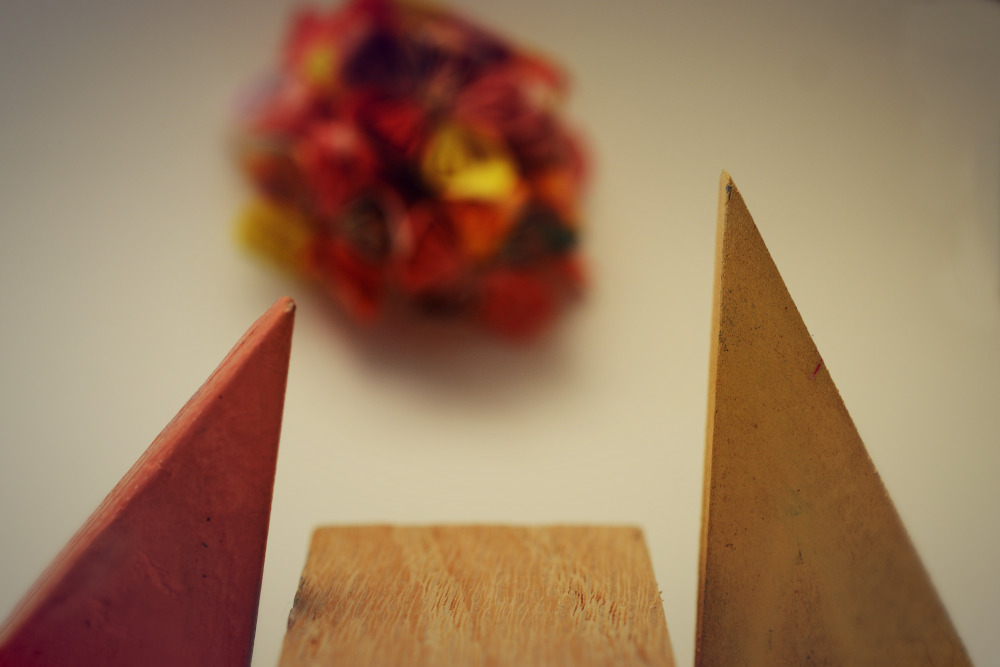 Two Block People on either side of a piece of wood for a table with a multi-colored puff ball above them.