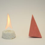 Block Woman stands next to a white circular cake-like object that has a single yellow flame above it.