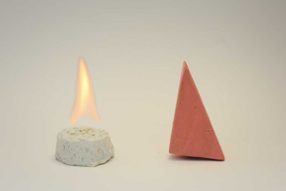 Block Woman stands next to a white circular cake-like object that has a single yellow flame above it.