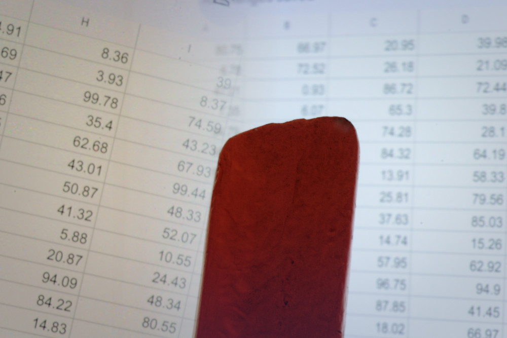 Block Woman looks at a spreadsheet on white paper with columns of black numbers